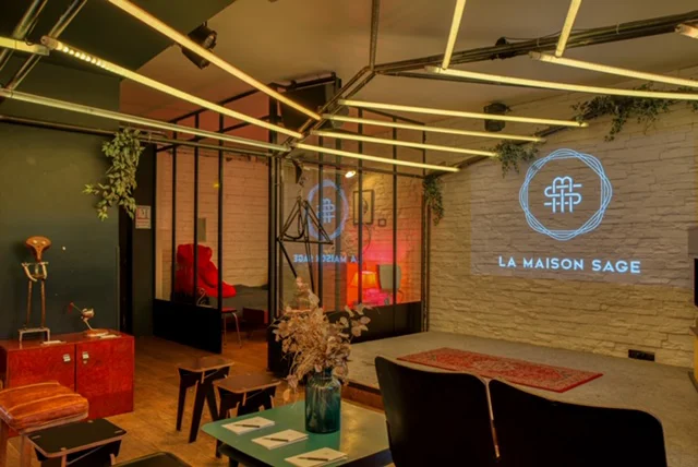 Espace lounge chaleureux avec tables, assises, plantes et mur de pierre.