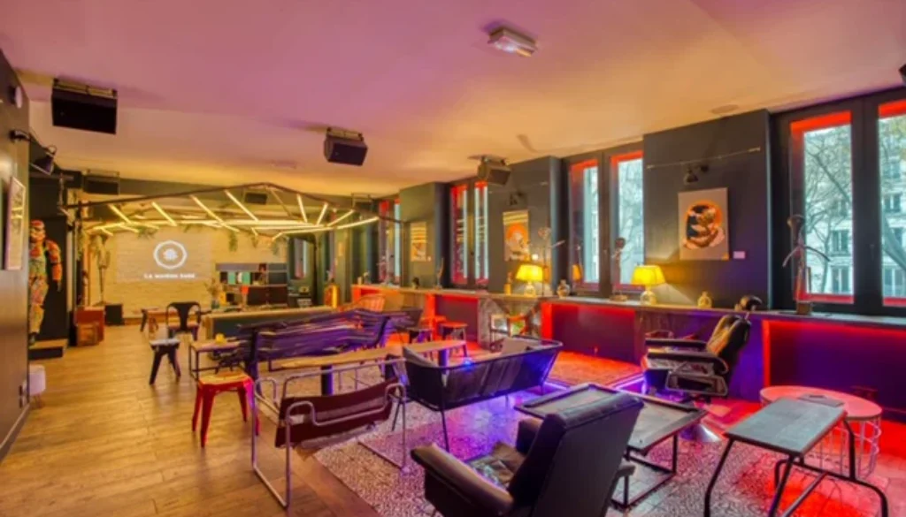 Espace lounge avec canapés, fauteuils, tables et écran au fond de la pièce.