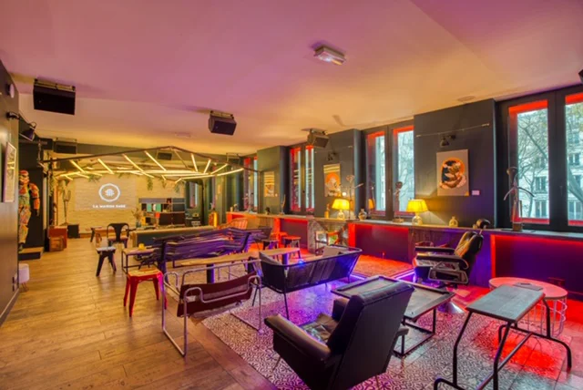 Espace intérieur avec canapés, fauteuils, tables et un écran visible au fond.