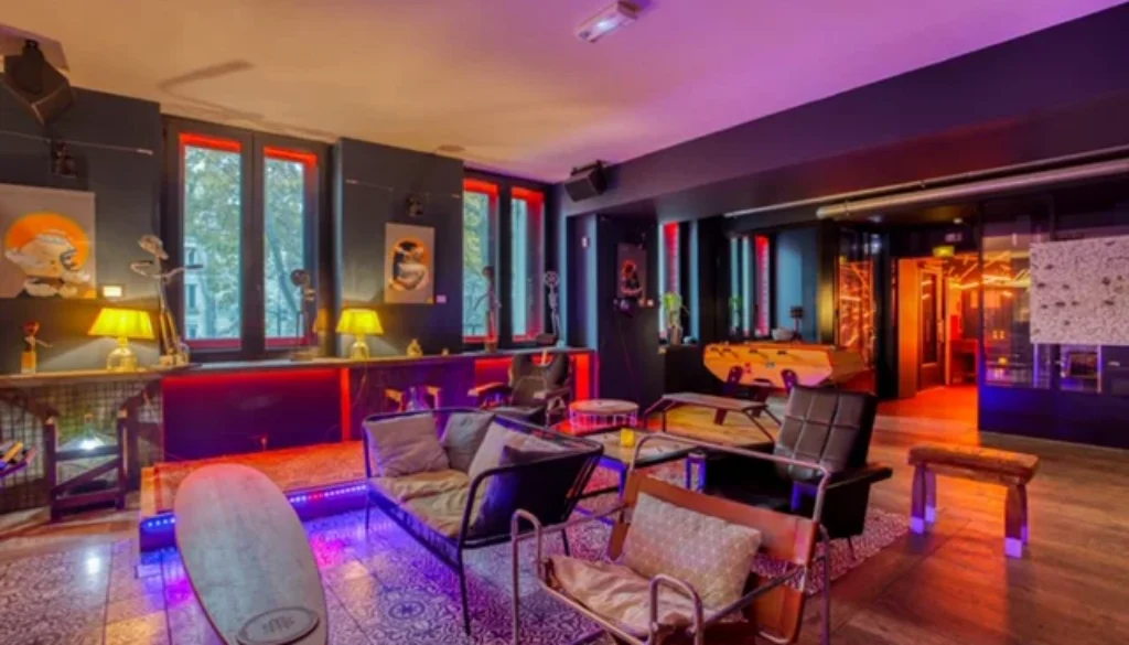 Salon intérieur avec fauteuils et canapés, grandes fenêtres et éclairage coloré.