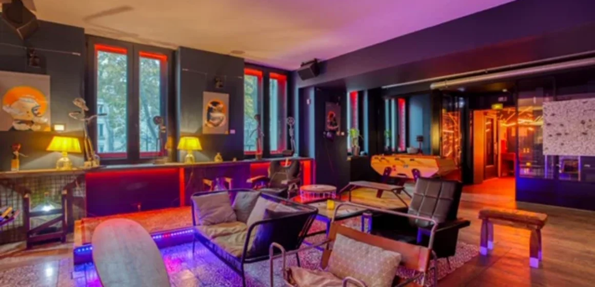 Salon intérieur avec fauteuils et canapés, grandes fenêtres et éclairage coloré.
