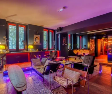 Salon intérieur avec fauteuils et canapés, grandes fenêtres et éclairage coloré.